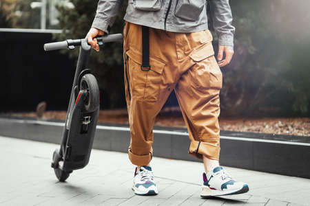 Close up of man holding electric kick scooter while going for a walk at street.の写真素材