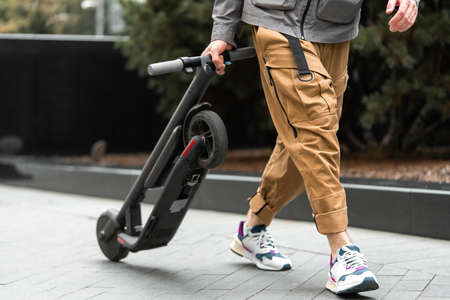 Close up of man holding electric kick scooter while going for a walk at street. light weight and...