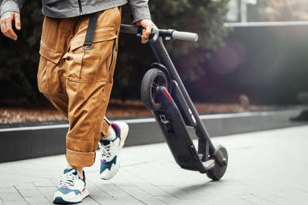Close up of man holding electric kick scooter while going for a walk at street.の写真素材