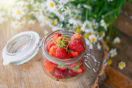 Glass Bowl with Fresh strawberry close up on rustic wooden table at countryside with camomiles on background.の写真素材