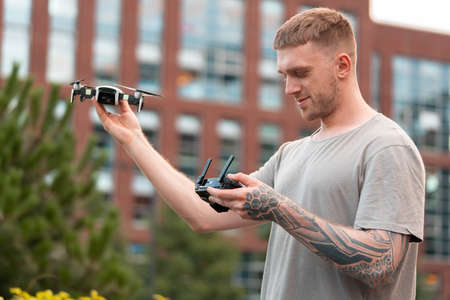 Young handsome man launching drone quadcopter at urban background. cityscape. modern device.