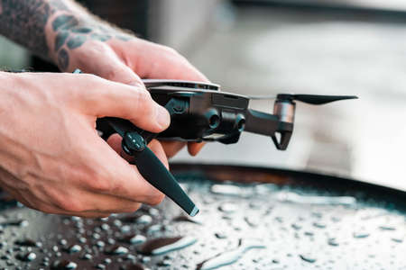 Close up of man folding drone quadcopter on wet black backgound. remote controlled wireless quadcopter drone with video and photo camera for aerial photographyの写真素材