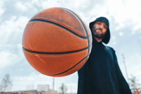 Close up of attractive man holding basket ball. Ball is on focus and foreground. Training outdoorの写真素材