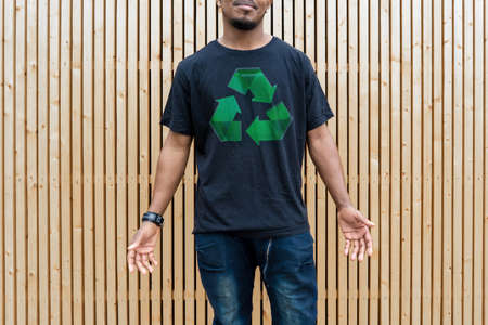 Young attractive man in black t-shirt with recycle symbol on wooden background. Eco symbol. Minimalismの写真素材