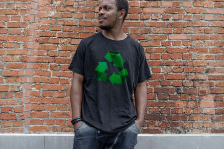 Young attractive man in black t-shirt with recycle symbol on brick background. Eco symbol. Minimalismの写真素材