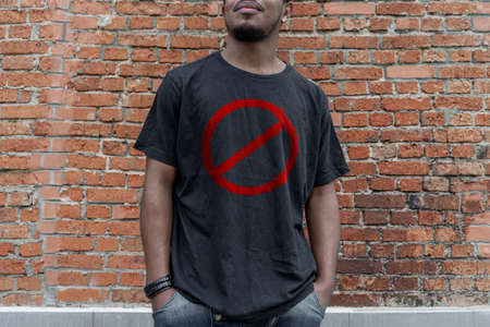 Young attractive man in t-shirt with forbidding prohibition stop symbol on brick background. Stop symbol. Minimalismの写真素材
