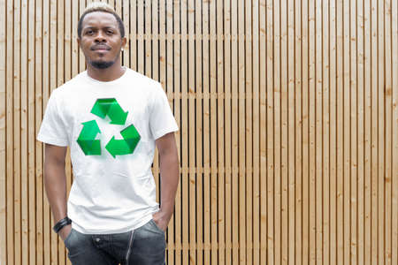 Young attractive man in white t-shirt with recycle symbol on wooden background. Eco symbol. Minimalismの写真素材