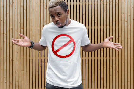 Young attractive man in t-shirt with forbidding prohibition stop symbol on wooden background. Stop symbol. Minimalismの写真素材