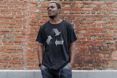 Young attractive man in black t-shirt with recycle symbol on brick background. Eco symbol. Minimalismの写真素材