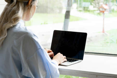 Young and pensive attractive woman working on laptop in modern library with big windows. Freelance concept. Young successful entrepreneur.の写真素材