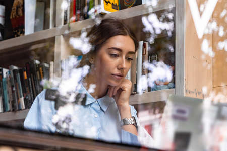 Young and pensive attractive woman working on laptop in modern library with big windows. Freelance concept. Young successful entrepreneur.の写真素材