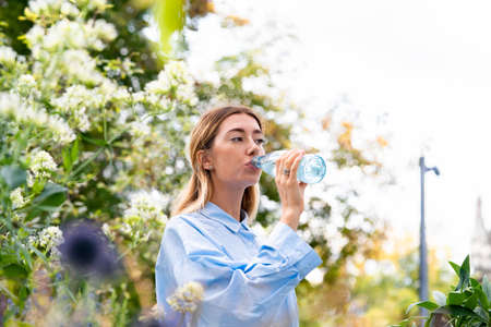 Young and attractive woman drinking sparkling water from glass eco biodegradable bottle at modern park. Eco friendly concept..の写真素材