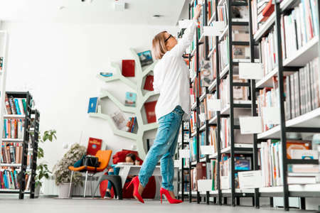 Young attractive pensive woman drawing hand to a book in a book store or library. Woman is on focus....