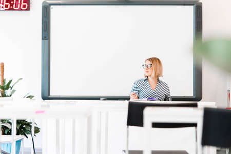 Young pensive attractive professor with glasses in formal clothes teaching at class and to take an...