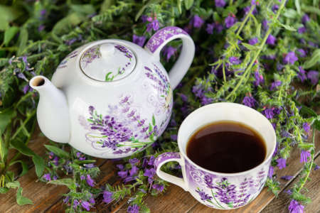 Close up of tea cup and teapot with violet petals and flowers on wooden Rustic tableの写真素材