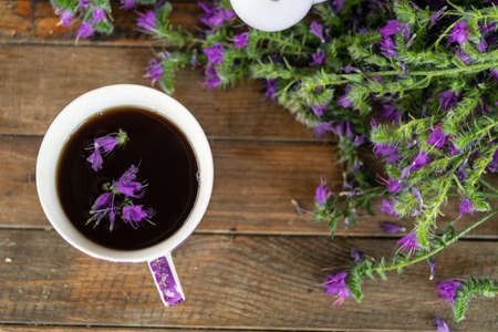 Close up of tea cup with violet petals and flowers on wooden table.の写真素材