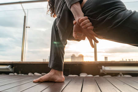 Attractive handsome athletic man practicing yoga in business center with beautiful view on a city from skyscraper. BusinessMan relaxing and meditating at dinner time or break. Peaceful and calming sunsetの写真素材