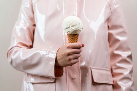 Close up of woman in pink raincoat holding vanilla ice cream in waffle cone. Minimalism concept.の写真素材