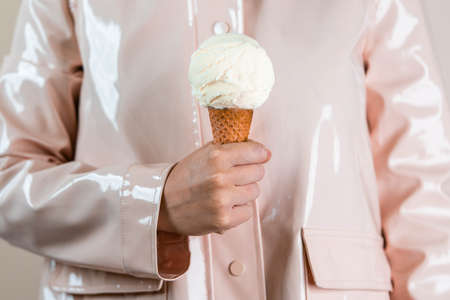 Close up of woman in pink raincoat holding vanilla ice cream in waffle cone. Minimalism concept.の写真素材