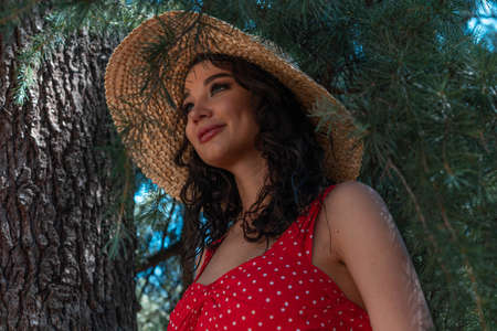 Young beautiful woman in red pin up dress and straw hat sitting on wood branch and smiling, Summer european vacation.の写真素材