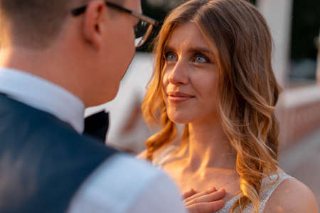 Wedding couple looking at each other with love and happiness at park at sunset time. Beautiful bride with groom. Female and male portrait.の写真素材