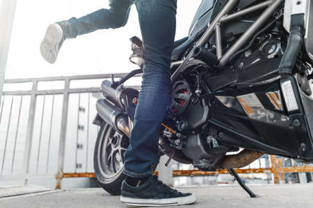 Close up of biker wearing sneakers and sitting down on motorcycle at parking.の写真素材