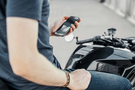Close up of biker holding mobile phone while sitting on motorcycle. Side view.の写真素材