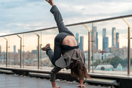 Attractive athletic man practicing yoga in business center with beautiful view on a city from skyscraper.の写真素材