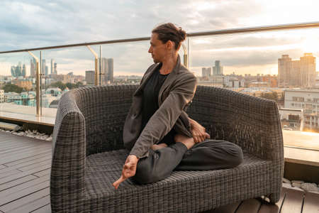 Attractive athletic man practicing yoga in business center with beautiful view on a city from skyscraper.の写真素材