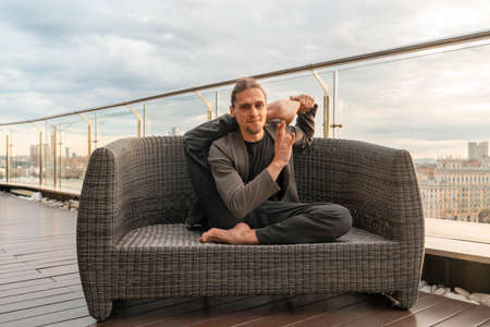 Attractive athletic man practicing yoga in business center with beautiful view on a city from...