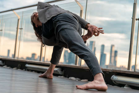 Attractive athletic man practicing yoga in business center with beautiful view on a city from skyscraper.の写真素材