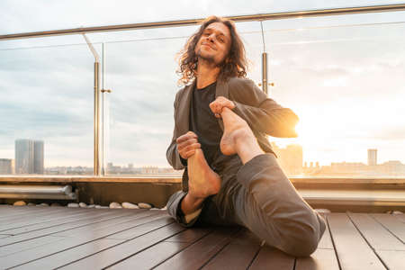 Attractive athletic man practicing yoga in business center with beautiful view on a city from skyscraper.の写真素材