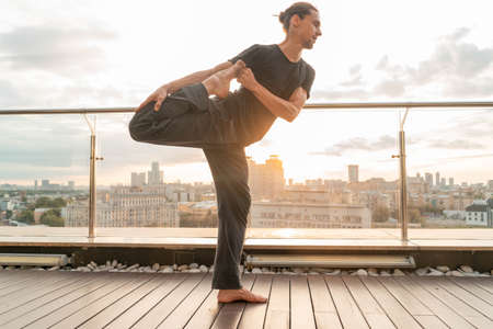 Attractive athletic man practicing yoga in business center with beautiful view on a city from skyscraper.の写真素材