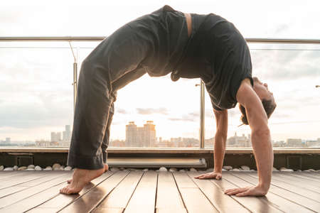 Attractive athletic man practicing yoga in business center with beautiful view on a city from skyscraper.の写真素材