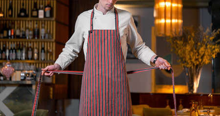 Young handsome cook chief tying apron in modern restaurant interior. Close upの写真素材