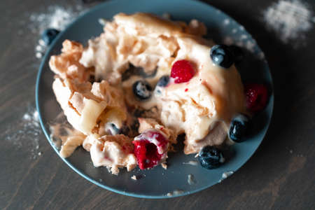 Pavlova Dessert Cake with Berries on grey Plate and wooden table. round Meringue with whipped cream, close up. Delicious Pavlova cake with fresh raspberry and blueberry.の写真素材
