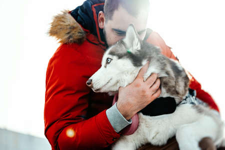 Man hugging Siberian Husky dog on a walk in modern park on sunny winter day. Human and animal pure Love. Best friend.の写真素材