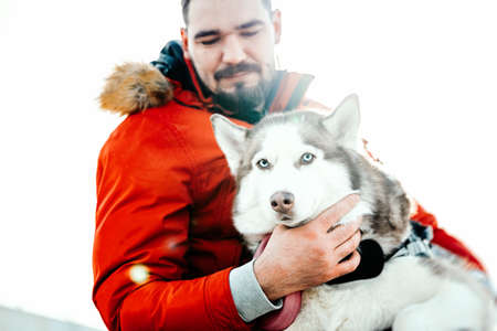 Man hugging Siberian Husky dog on a walk in modern contemporary park on sunny winter day. Human and animal Love and friendship concept. Life after shelter.の写真素材