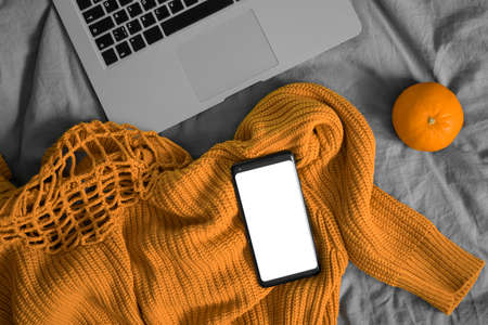 Mobile Phone With Blank Screen On Woolen Sweater Near Orange And Laptop. Copy Space. Empty Space.