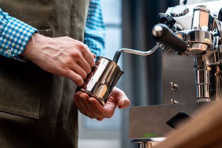 Barista Warming Milk In Metal Jug With Steam Of Coffee Machine. Cappucino Or Latte Coffee Preparation At Home. Quarantineの写真素材