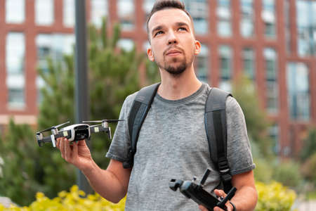 Young Handsome Brunette Man Launching Drone Quadcopter and Looking Above Viewer. Urban Stlilysh Contemporary Cityscape. Modern deviceの写真素材
