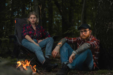 Beautiful Backpacker Woman And Man Having Rest Near Bonfire After Hiking In Forest. Contains chrominance noise, luminance noise, sharpening noise, or film grainの写真素材