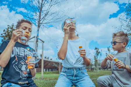 Young Stylish Mum and Two Sons Blowing Bubbles In The Park and Having Fun.の写真素材