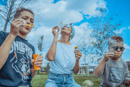 Young Stylish Modern Mum and Two Sons Blowing Bubbles In The Park and Having Fun.の写真素材