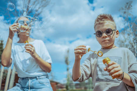 Young Stylish Modern Mum and Two Sons Blowing Bubbles In The Park and Having Fun.の写真素材