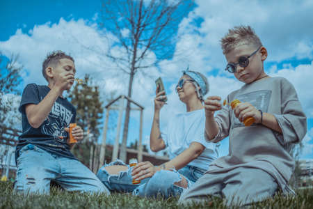 Young Stylish Modern Mum and Two Sons Blowing Bubbles In The Park and Having Fun.の写真素材