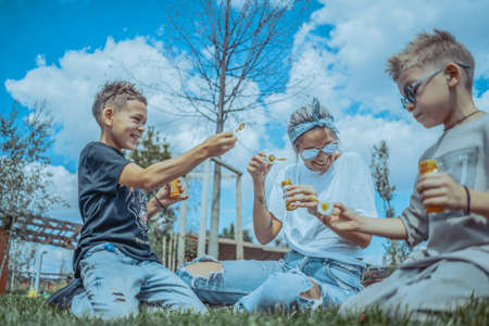 Young Stylish Modern Mum and Two Sons Blowing Bubbles In The Park and Having Fun.の写真素材