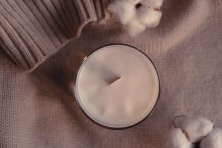 Top View Of Scented Candle And Cotton Flower On Cozy Stylish Sweater. Candle In Glass With Blank White Label.の写真素材