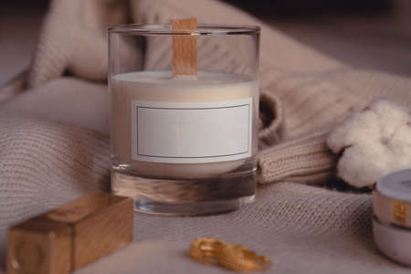 Composition Of Scented Candle, Cozy Stylish Sweater. Cotton Flower, Lipstick, Earrings And Powder. Candle In Glass With Blank White Labelの写真素材