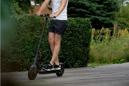 Close Up Of Man Riding Electric Kick Scooter At Beautiful Park Landscape. Man Is On Foreground, Modern Park is on Background And Blurred.の写真素材